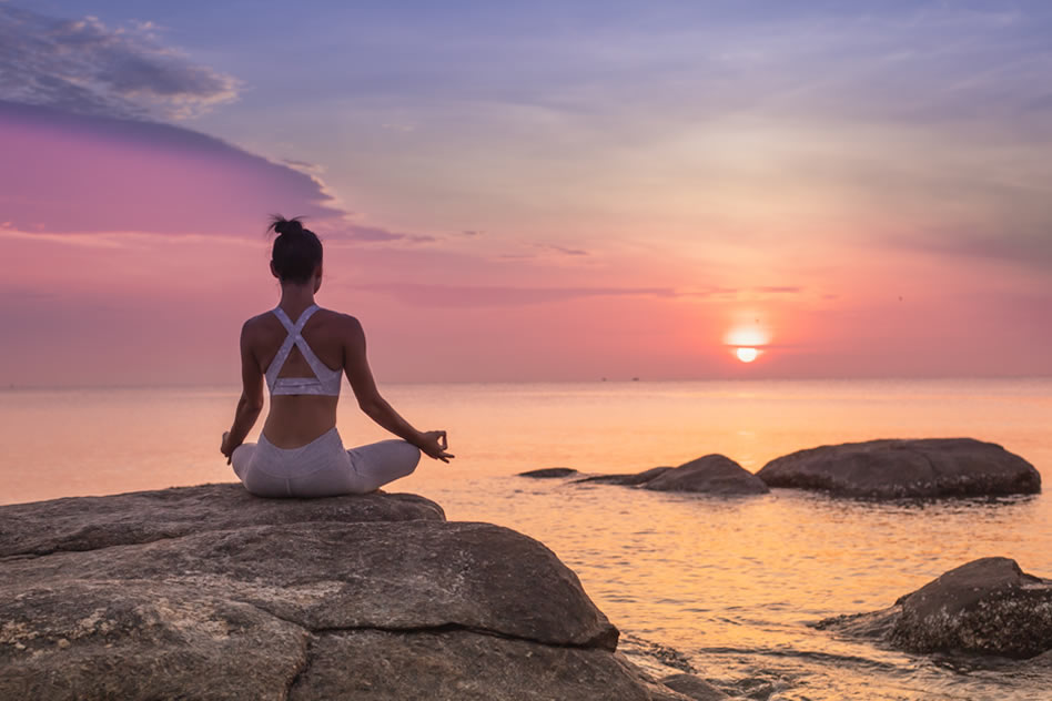 Mujer observando el atardecer mientras practica hatha yoga al aire libre